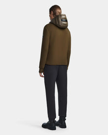 A person with long hair, facing away, wears the Rudsak DURIN S - M123518 mens hooded jacket in light olive with lightweight down insulation, paired with black pants and shoes against a plain light background.