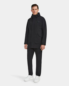 A man stands against a plain background wearing the Rudsak IAN - 6124009 Black rainwear jacket, black pants, and white sneakers, looking forward with a neutral expression.
