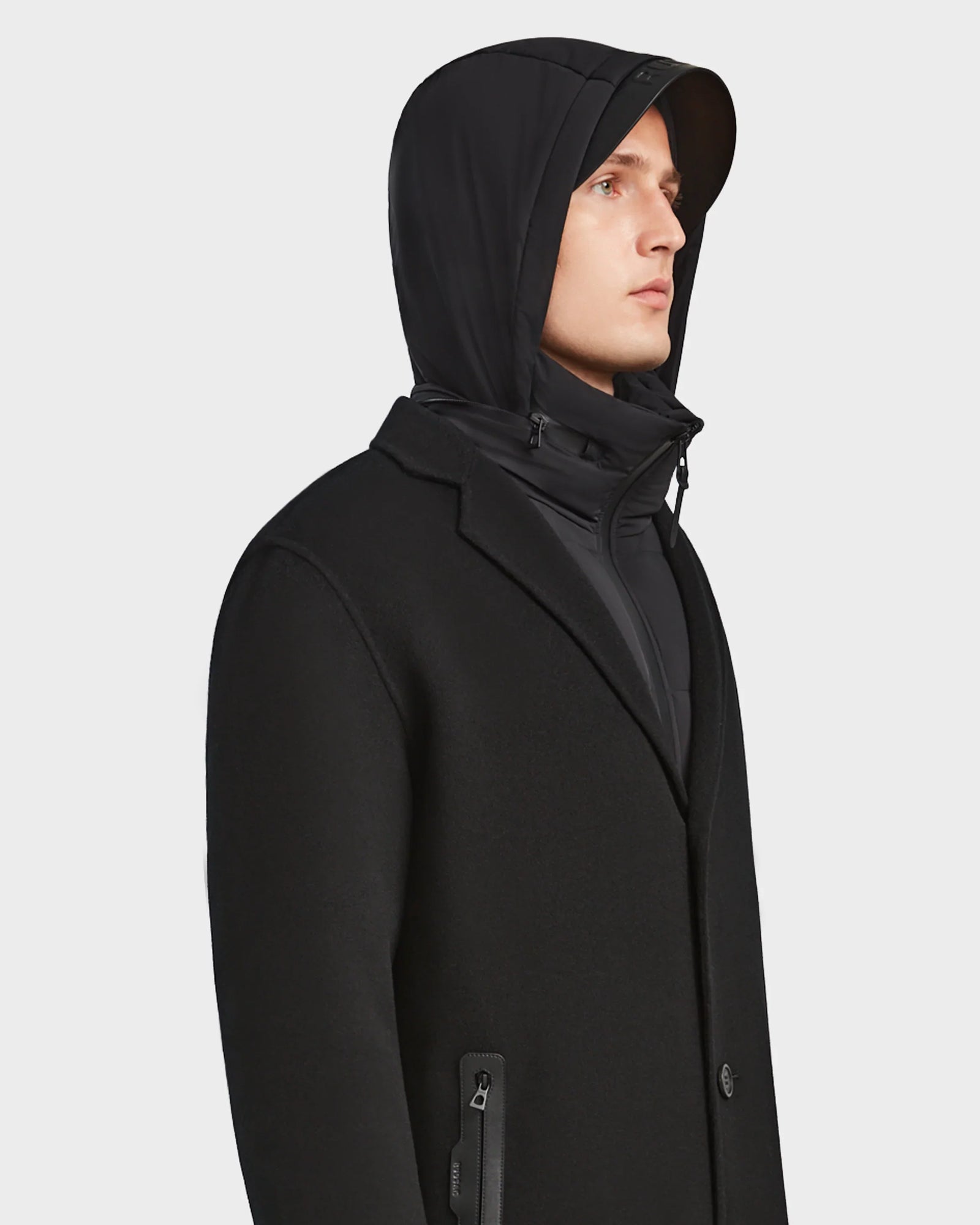 A man wearing the Rudsak DRAL - 6124503 Black wool jacket with a high collar and a black hooded layer beneath, looking to the side against a plain white background.