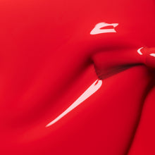 A close-up of glossy red paint with a smooth texture, featuring a shiny, reflective surface and a subtle swirl or indentation near the center.