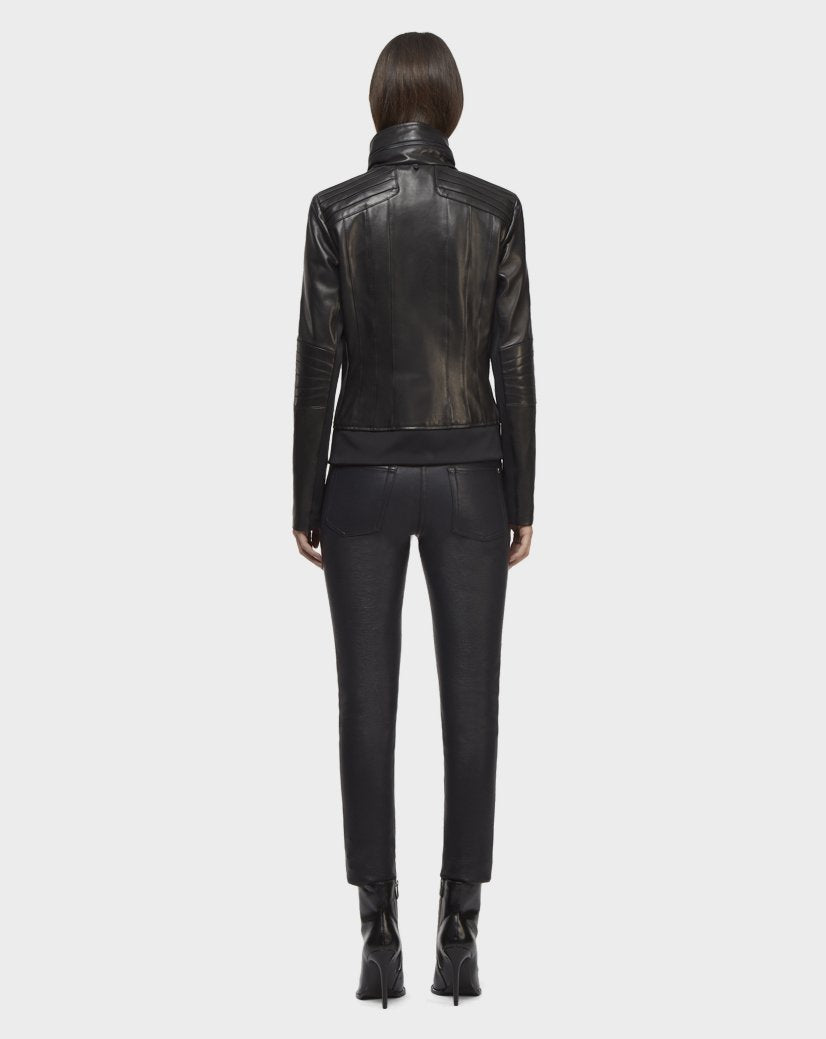 A person with straight, shoulder-length hair faces away, wearing the Rudsak PRESLEY - CA EN 8119029 BLACK biker jacket, paired with black pants and heeled boots, standing against a plain light background.
