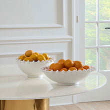Two white ceramic bowls filled with oranges on a white surface with a window in the background.