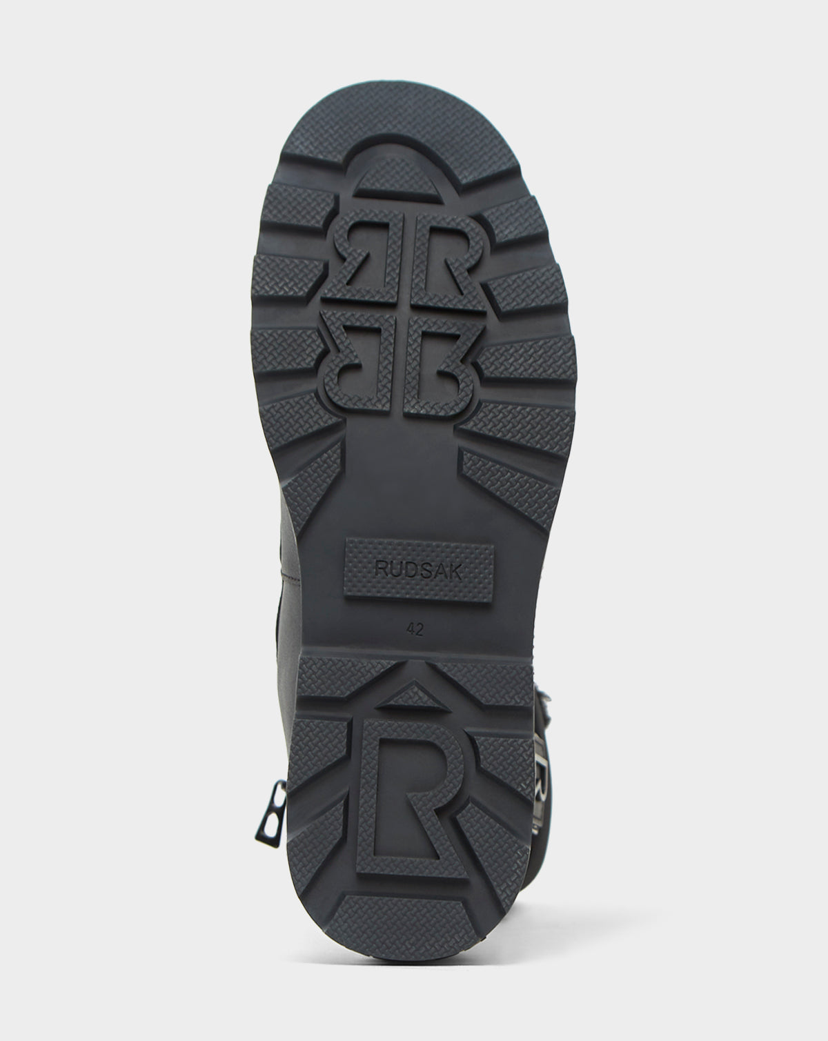 The image shows the black rubber sole of the Rudsak REAGAN - 6222500 BLACK men’s boot, featuring deep treads with raised R logos, the brand name, and size 42 embossed in the center.