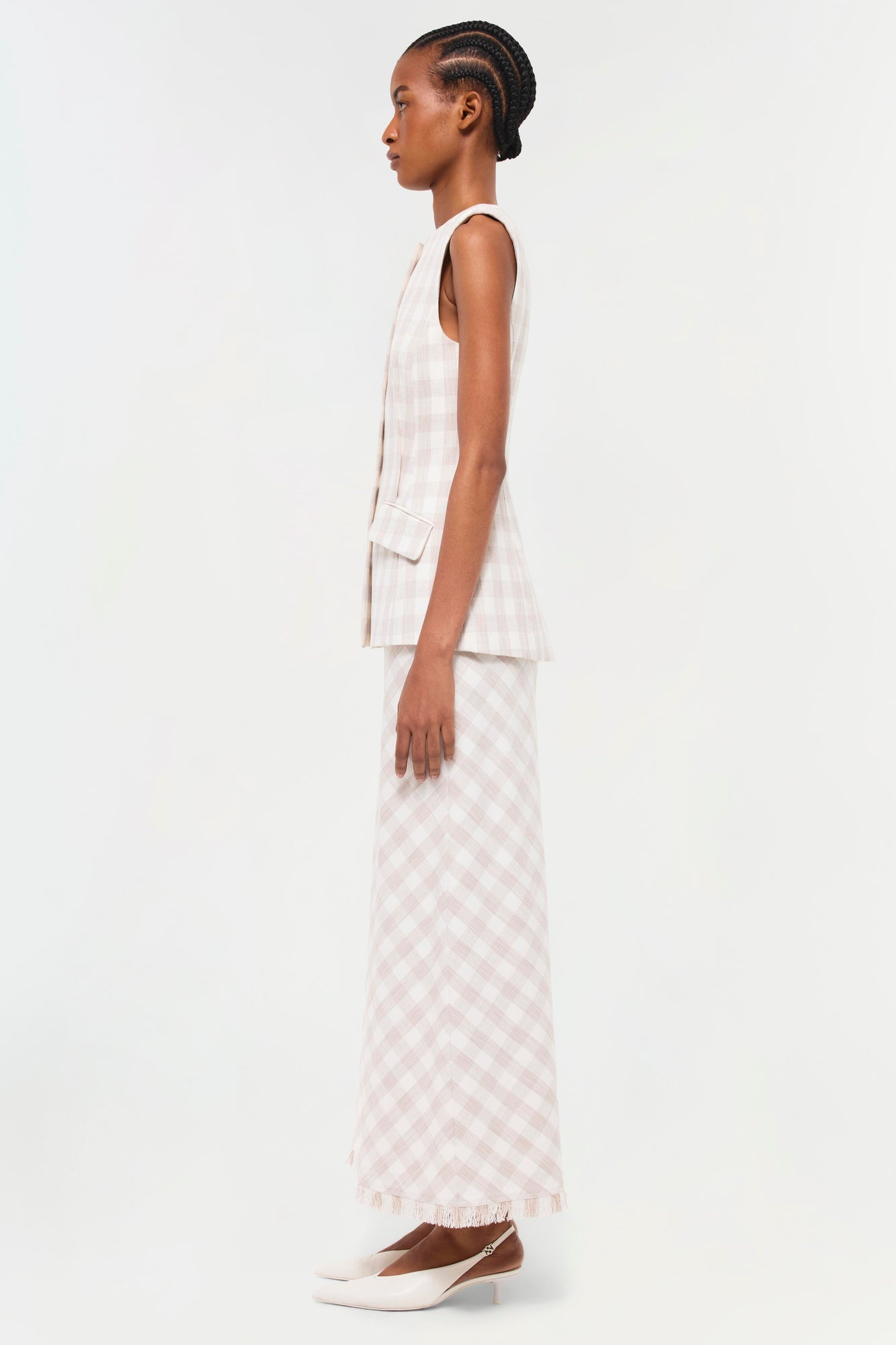 Sleeveless cream vest with vertical pleats and patch pocket, styled with gingham maxi skirt and white platform shoes.