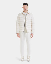 A man faces forward against a plain white background, wearing Rudsak’s AZIEL - M124521 Vanilla puffer shirt jacket, paired with white pants, a white top, and white sneakers.