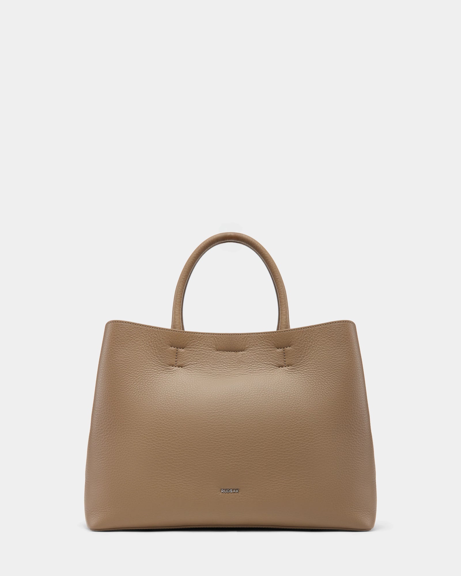 The Rudsak CATIRA L - 8325007 Almond is a taupe leather womens tote with a pebbled finish, two rounded handles, and a subtle metallic logo near the base, shown on a plain white background.