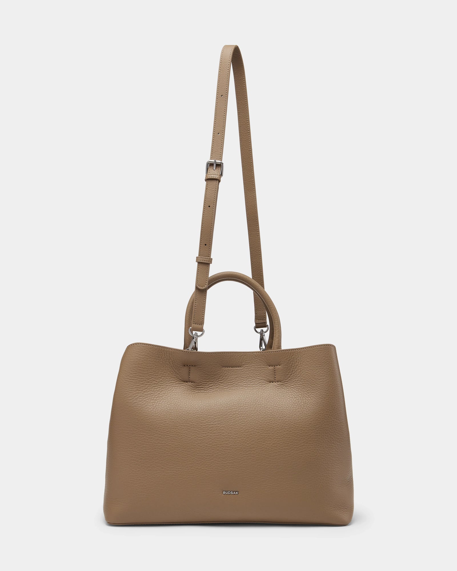 The CATIRA L - 8325007 Almond by Rudsak is a taupe women’s leather tote with double handles, a long adjustable strap, and a minimalist design featuring a small metallic logo—perfect as a versatile statement accessory.