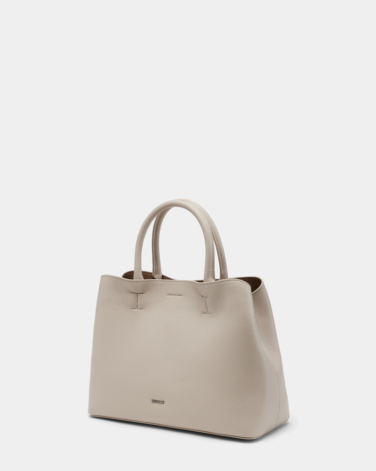 The Rudsak CATIRA S - 8325006 Vanilla is a large, light beige womens pebble leather tote with two rounded handles, subtle textured finish, minimal branding near the bottom, and is shown against a plain white background.