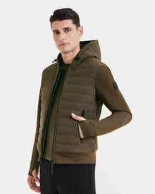 A man wears the Rudsak DEE MAT - 6124028 Army, a mens lightweight down jacket with zippered pockets, standing against a plain white background and looking slightly to the side with one hand in his pocket.