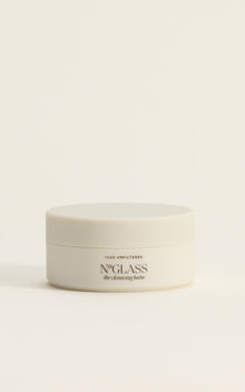 Small white jar labeled 'The Cleansing Balm — LUX UNFILTERED' on a neutral pale background