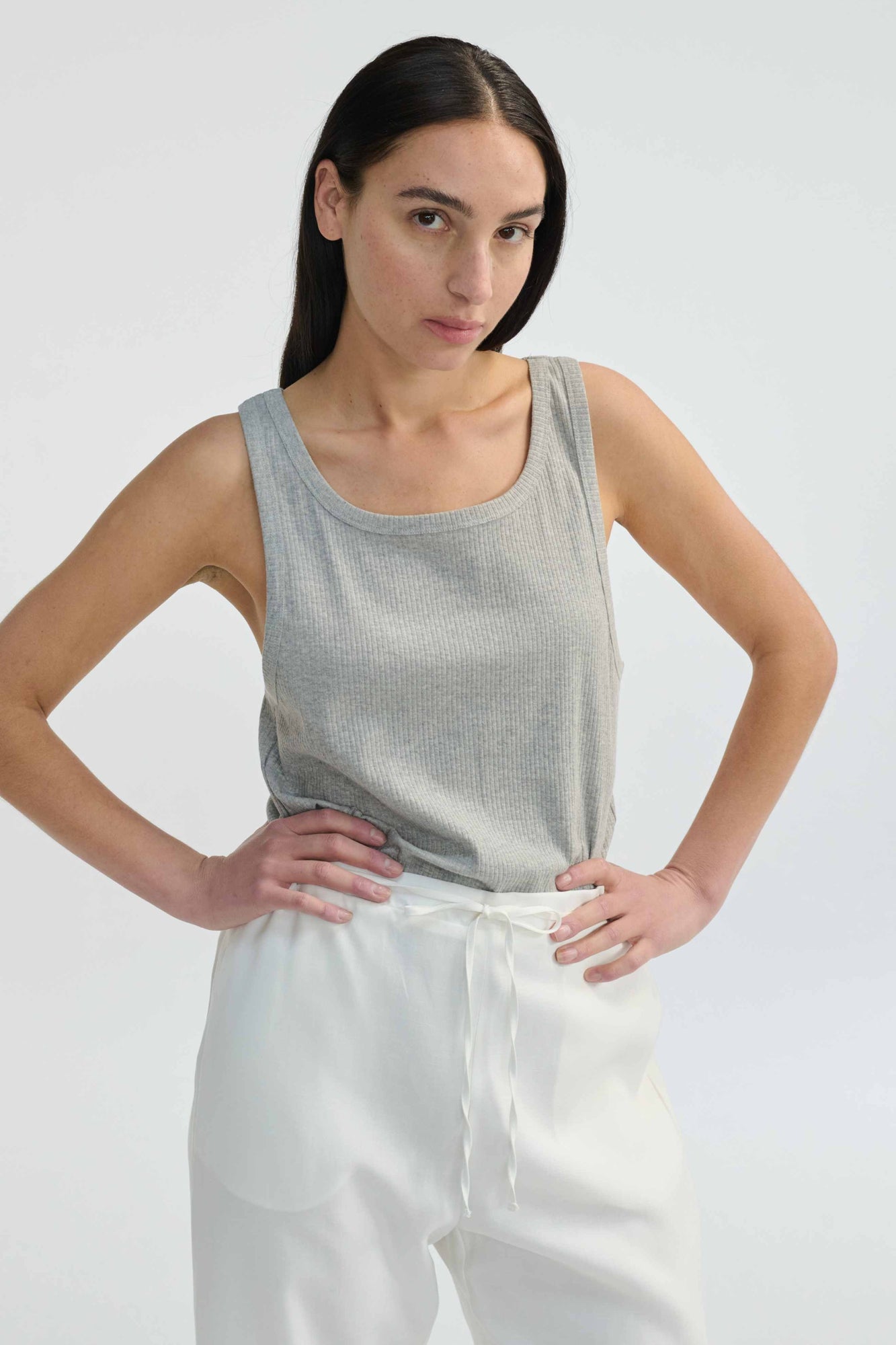 Woman wearing a gray tank top and white pants against a plain background