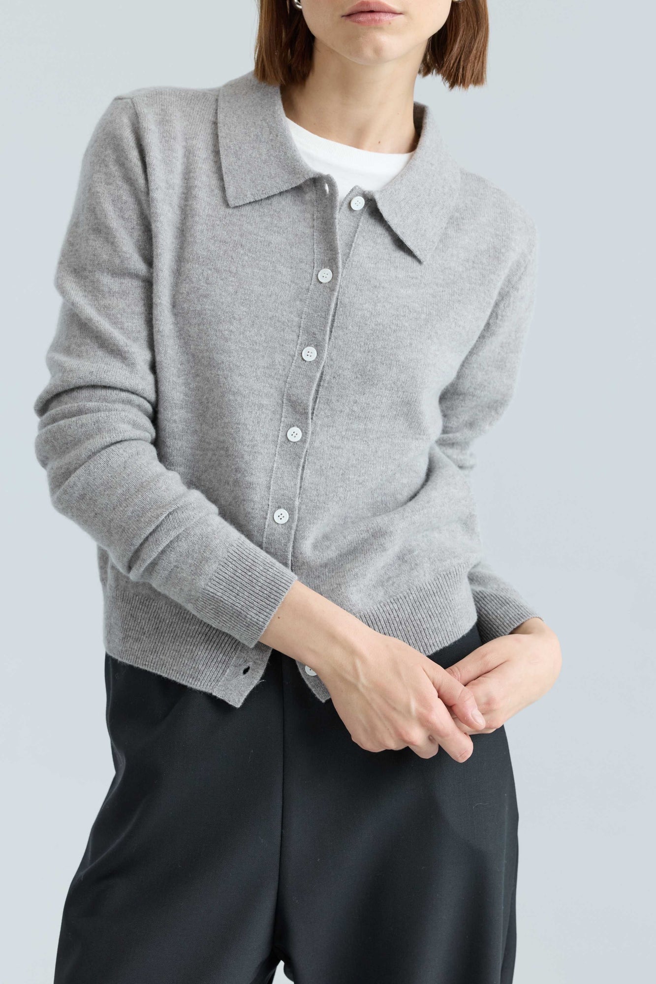 Person wearing a gray cardigan over a white shirt with black pants on a light gray background