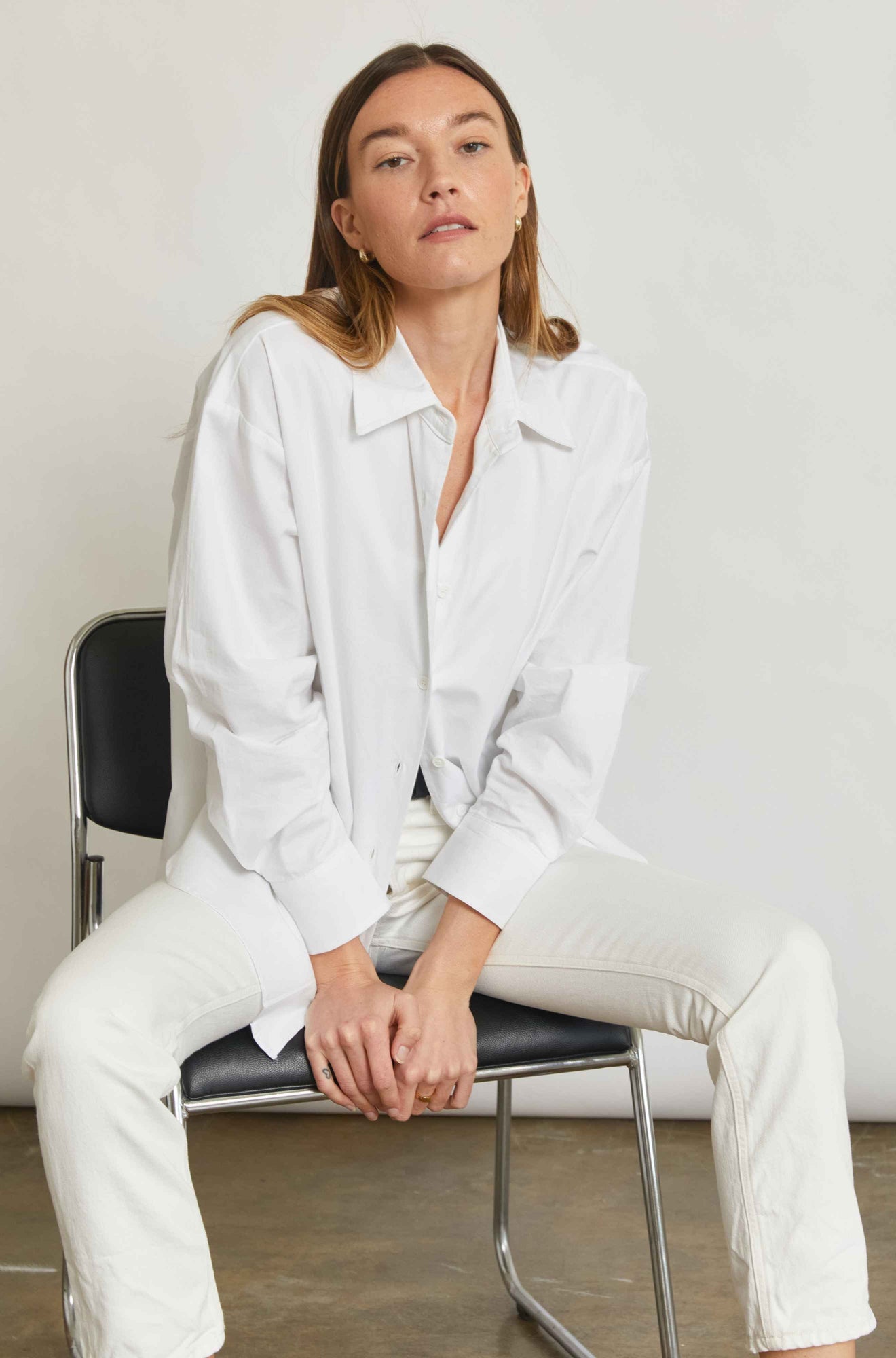 Woman wearing a white outfit sitting on a chair against a plain background