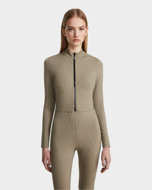 A woman with straight, light brown hair models the Rudsak SHANYA - 8523526 Cement Pattern, a fitted long-sleeve zip-up bodysuit in taupe stretch fabric with a subtle geometric pattern, against a plain light background.