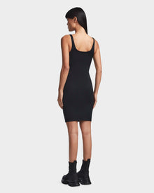 A woman with straight dark hair faces away, wearing the Rudsak MILEY - 8523034 BLACK bodycon dress and black chunky boots with high socks, standing against a plain white background.