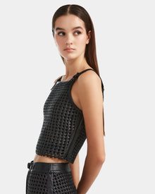 A young woman with straight brown hair models the NADINE - 8524042 Black by Rudsak—a handwoven cropped top with matching high-waisted bottoms—against a plain light background, embodying true luxury.