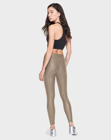 A woman stands facing away, looking over her shoulder. She wears a Rudsak SHIRIN L - 8521034 Cement animal-friendly legging with a black sports bra and metallic silver sneakers against a plain light gray background.