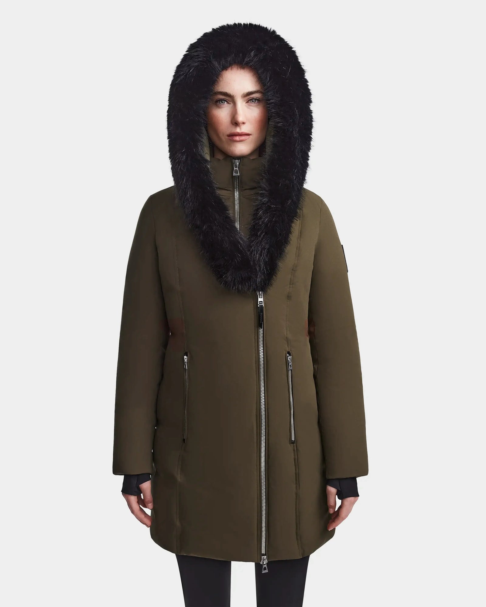 A person stands facing forward wearing the Rudsak MAIA M - 8123582 Army winter jacket with a large black faux fur-lined hood, zipped up, against a plain light background.