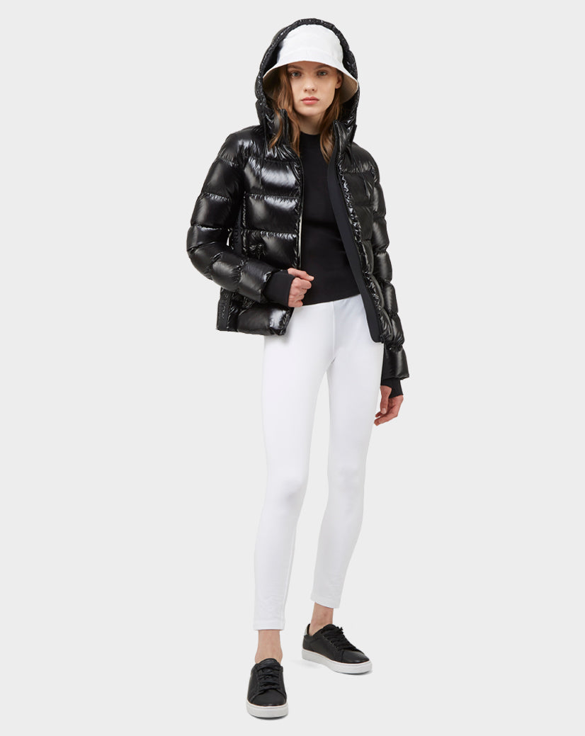 A woman faces forward against a plain light background, wearing the MARE - 8121011 BLACK women's down puffer jacket with a hood by Excluded, paired with a white baseball cap, black top, white fitted pants, and black sneakers.