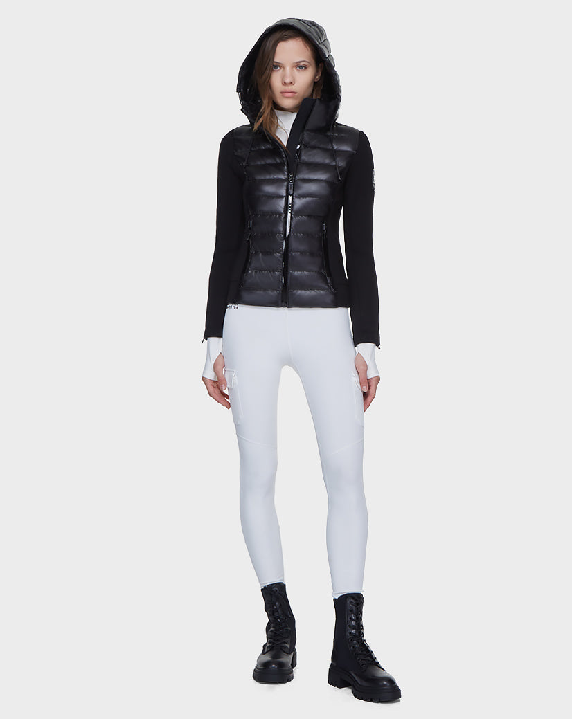 A woman faces forward wearing the Rudsak MABS - 8121012 BLACK lightweight activewear jacket with waterproof zippers, paired with white fitted pants and black combat boots against a plain white background.