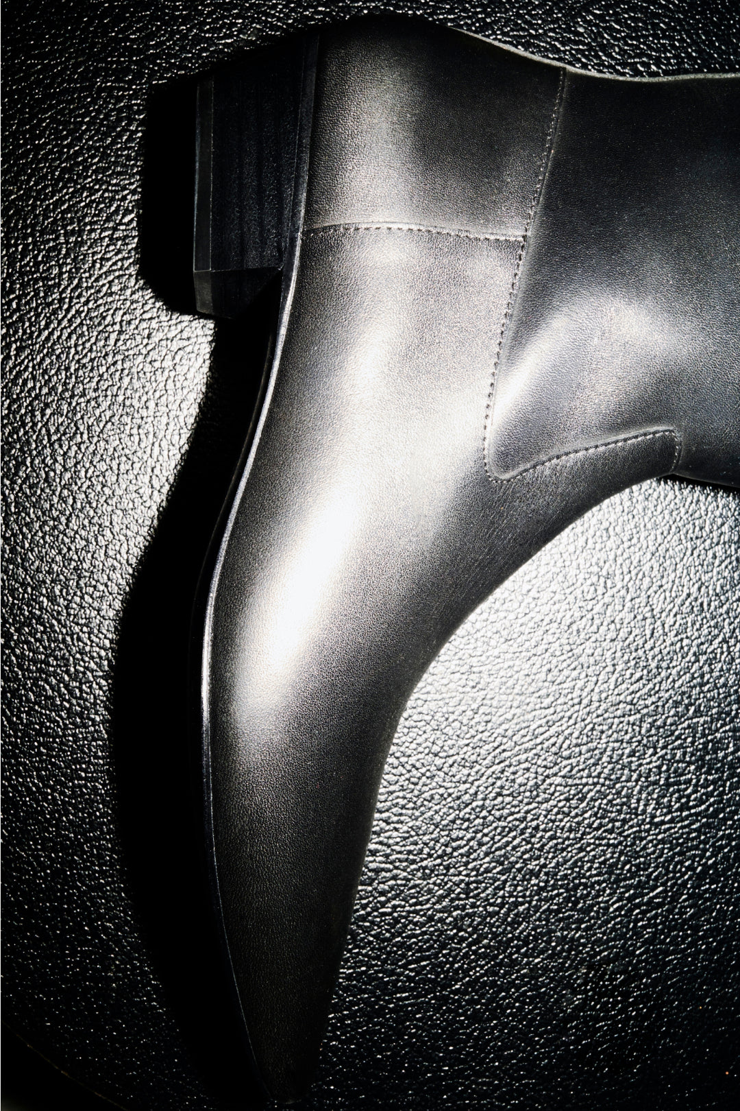 Black leather riding boot with stitched seams and smooth finish, shown in profile against textured background.