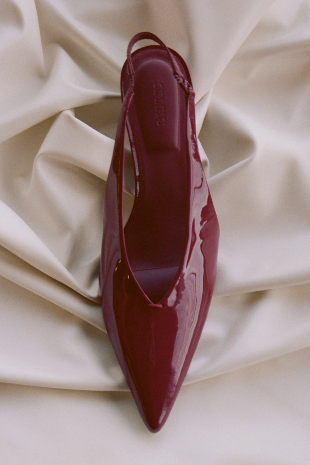 Burgundy slingback kitten heel shoe with pointed toe, displayed from above on cream fabric.