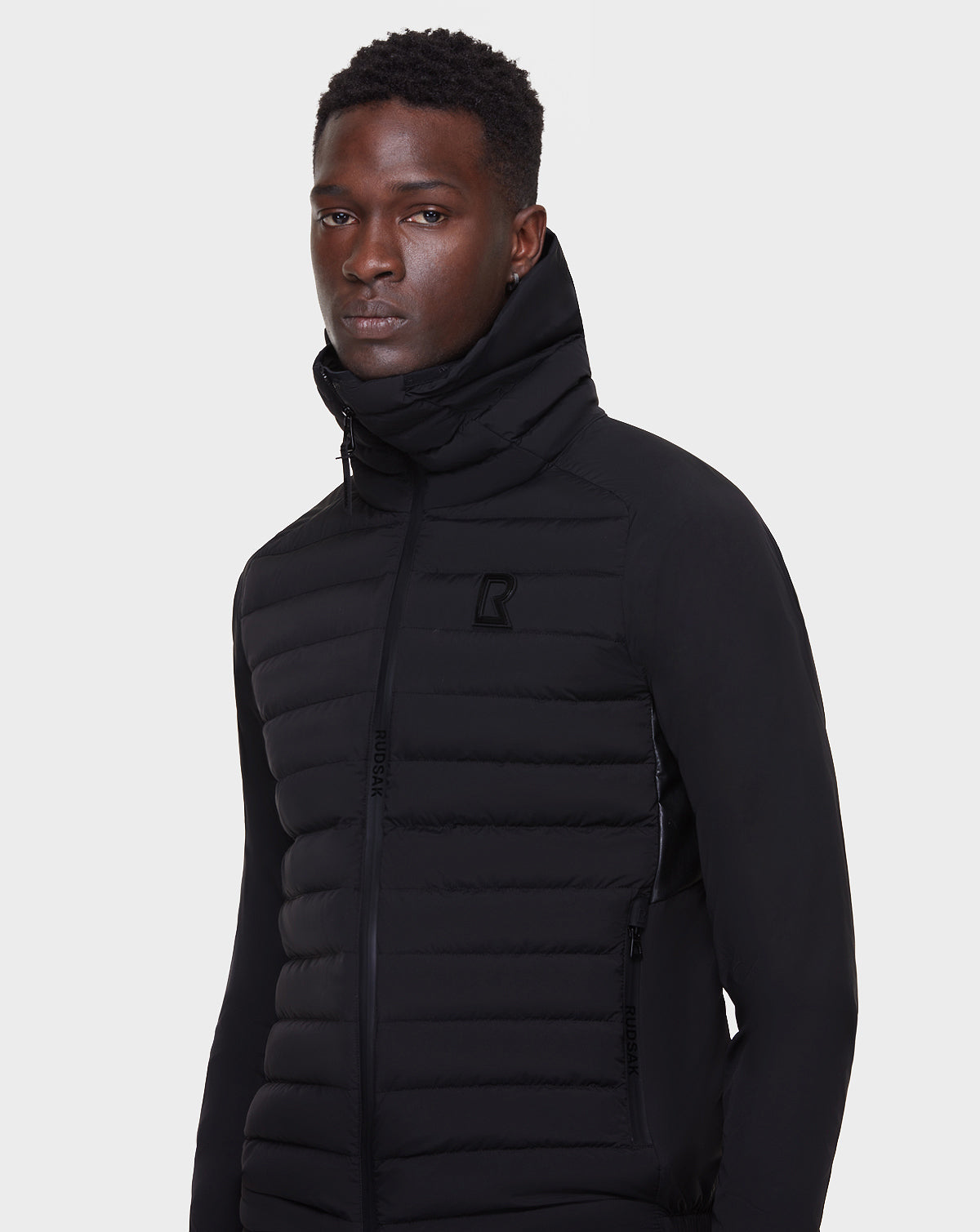 A man wearing the RUDSAK JARRY - 6122007 BLACK quilted zip-up mens windbreaker with a high collar, standing against a plain white background and looking slightly to the side.