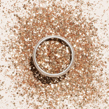 A silver ring rests on a surface dusted with Manucurist Glitters Duo Rose Gold  Glazed, creating a sparkling background with hints of rose gold and glazed shimmer.