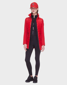 A woman faces forward in a Rudsak MERINA - 8121006 POPPY RED quilted down jacket, red baseball cap, black zip-up top, leggings, and sneakers against a plain light background.