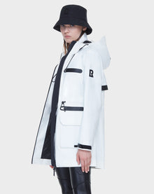 A person models the Rudsak CAMY - 8122002 WHITE mid-length raincoat, featuring black zippers, paired with a black bucket hat and pants against a light background, facing slightly to the side.